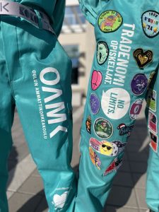 Kaksi henkilöä poseeraa turkoosit OUTO RY:n haalarit päällä ulkona. Toisissa haalareissa on haalarimerkkejä.