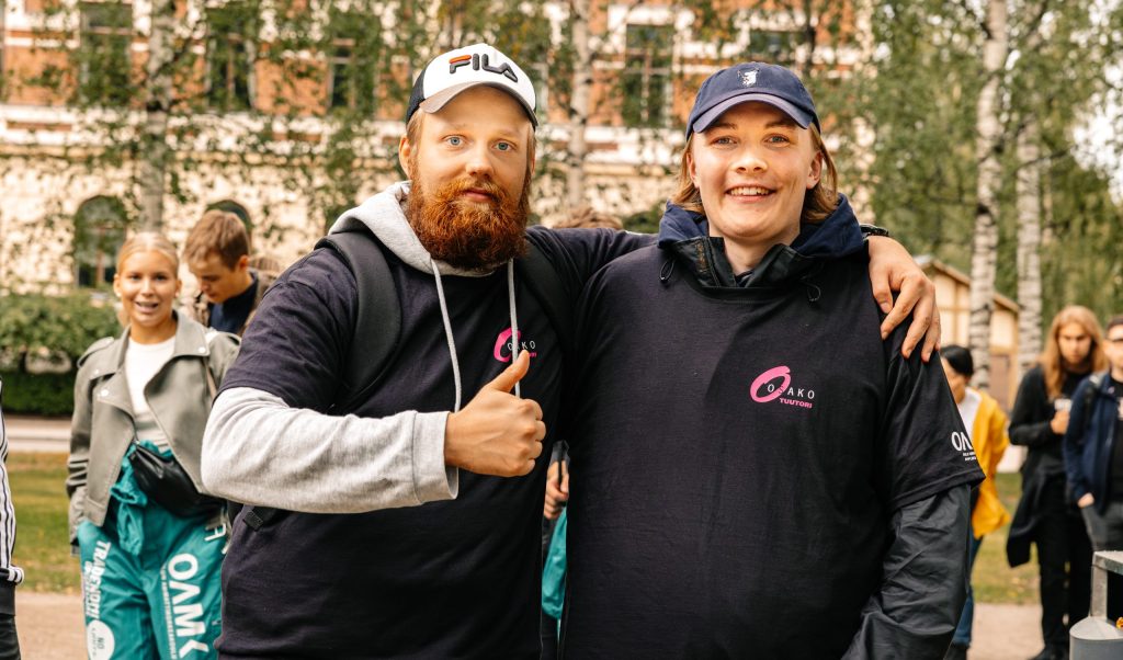 Kaksi henkilöä poseeraa Osako-tuutoripaidoissa ulkona.